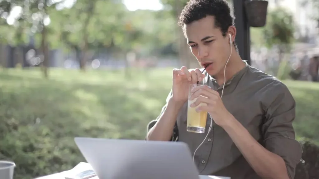 Man drinking lemonade in cafe while using laptop at a Phone Charging Station Rental.