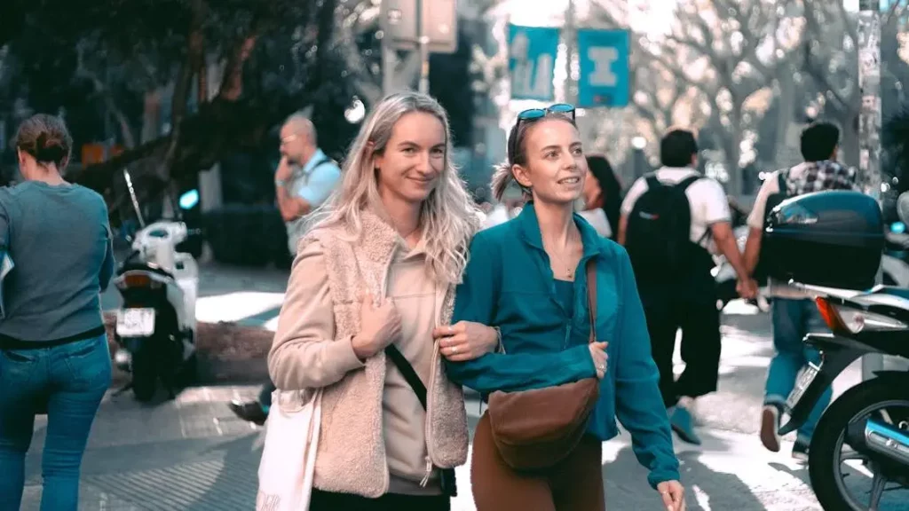 Women passing Phone Charging Kiosks on a sunny urban street day.