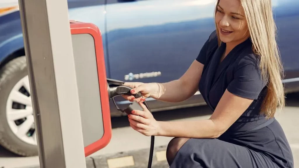 Positive female using phone charging kiosk on street while charging electric vehicle