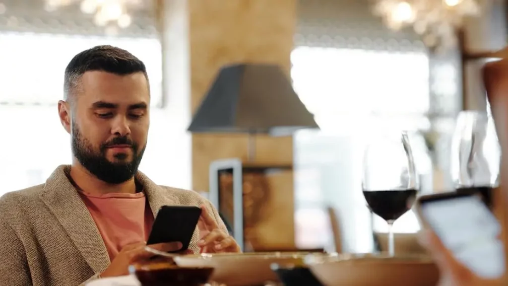 Mobile Charging Solutions Help Restaurants: Man using smartphone at restaurant table with wine glass