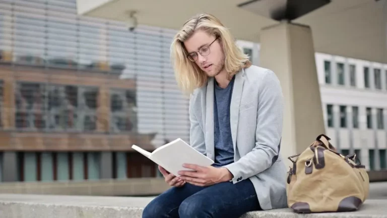 Young man reading on a campus bench next to Phone Charging Kiosks.