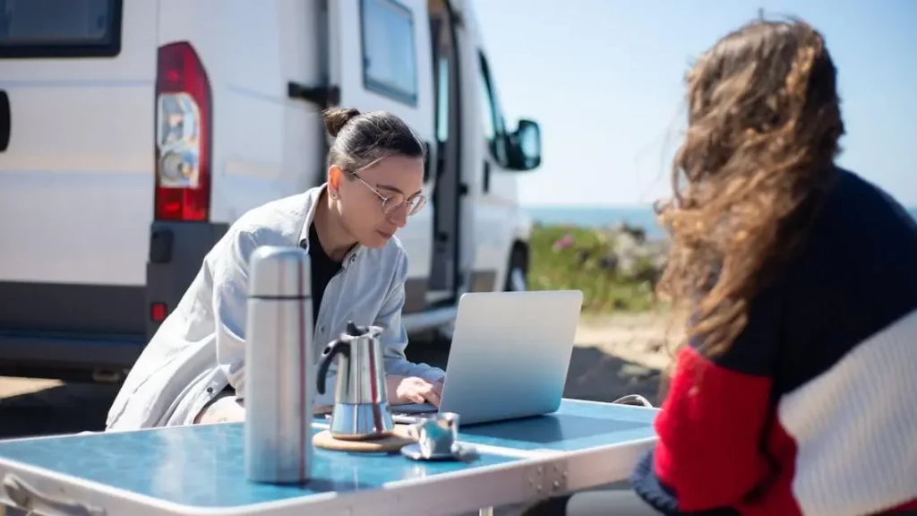 Adults using a laptop near a camper van, highlighting "Portable Charging vs. Fixed Charging Stations: Which Fits Your Needs?"