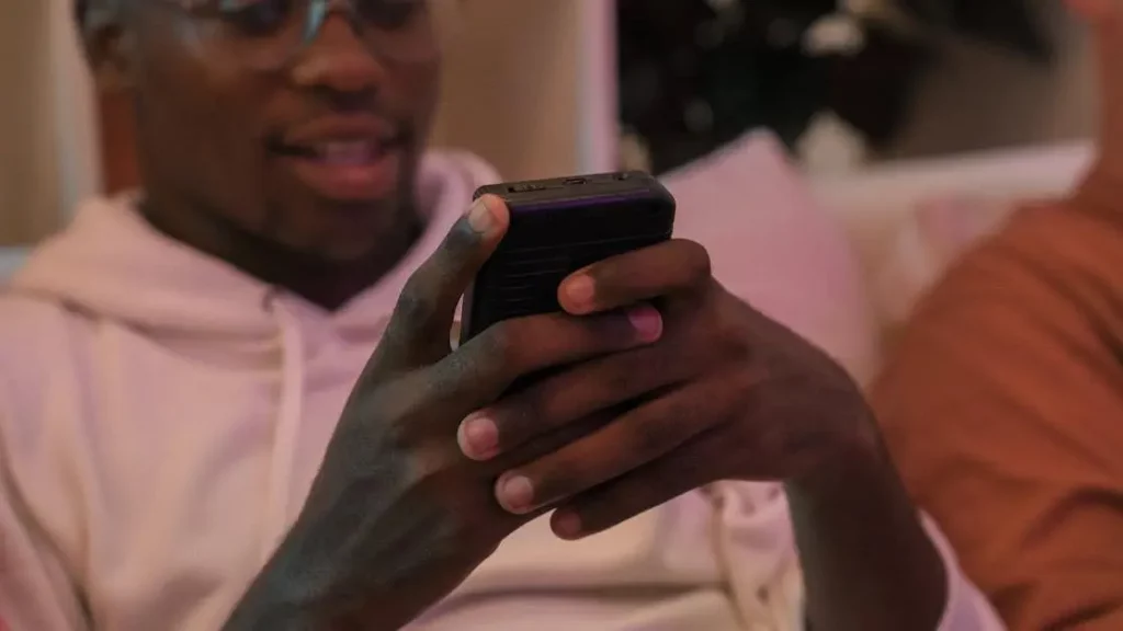 Man using smartphone with friends indoors; demonstrates how portable chargers help venues boost brand loyalty.