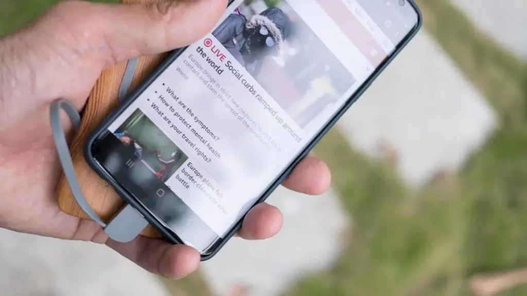 Smartphone charging with a portable power bank while browsing news; focus on portable charging in public spaces.