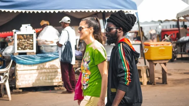 Cheerful couple explores Accra market, immersing in local culture to enhance the visitor experience.